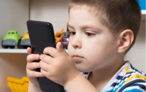 A young boy holding a phone very close to his face because of myopia (extreme nearsightedness)