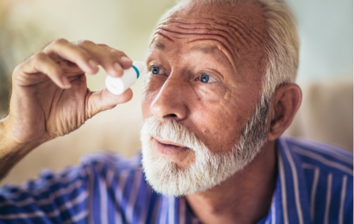 An older man using his right hand to place medicated eye drops into his right eye to help treat his tunnel vision