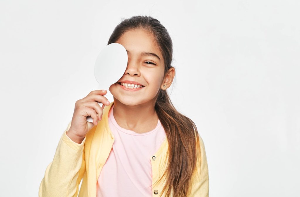 A young girl is standing against a grey background covering her right eye for a visual acuity test