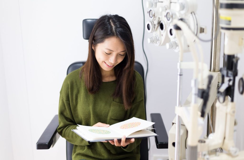 A young woman sitting at the optician testing chair is  reading an Ishihara Colour Vision Test Book for testing color blindness