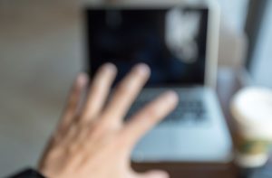 An image depicting blurry vision and what it would look like from a first person perspective. The person is reaching their hand out towards their laptop, but it's blurry.