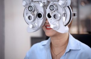 An optometrist examines a female patient's eyes while she sits behind a phoropter at the eye doctors office