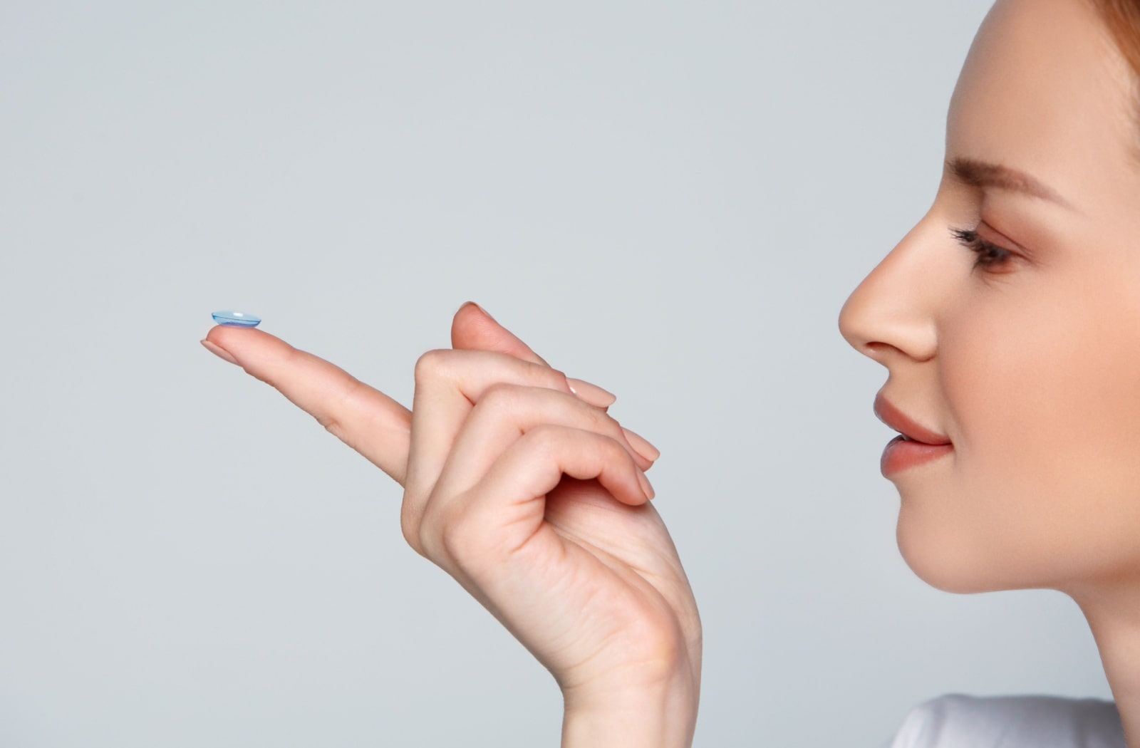 A woman holding out a contact lens on her index finger