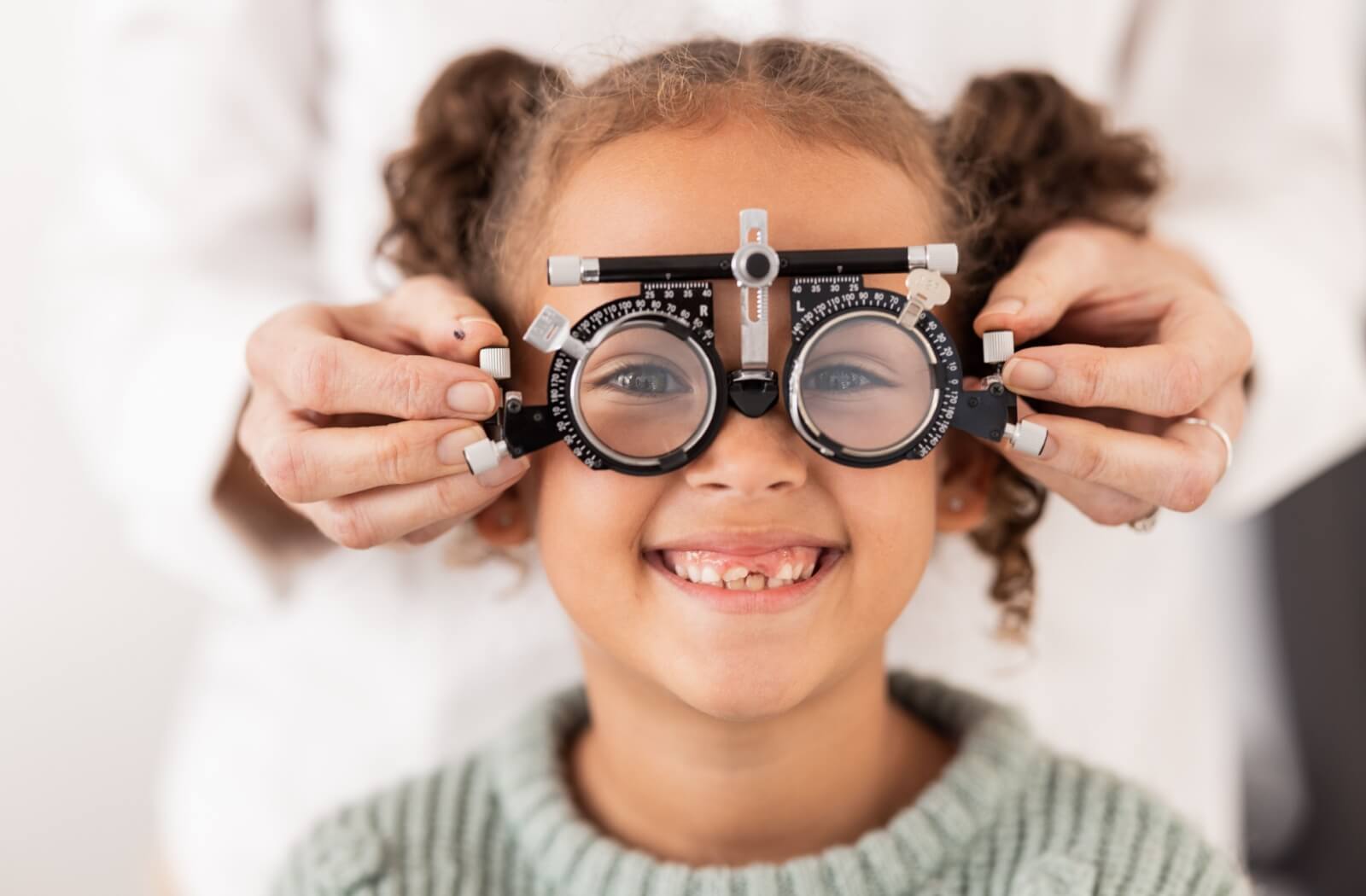 Cute smiling child undergoing an eye exam with an eye doctor behind her.