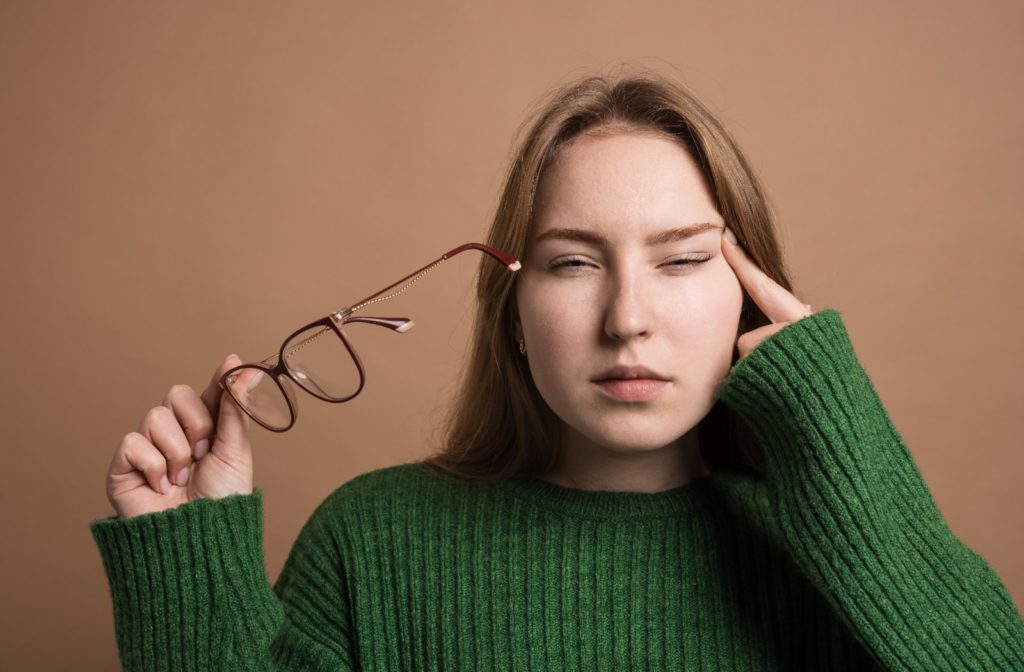 Young woman experiencing eye strain caused by astigmatism while holding her glasses.