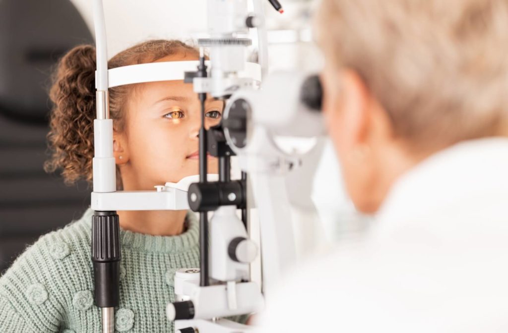 A child in a green sweater receiving an eye exam from an eye doctor to assess eye health.