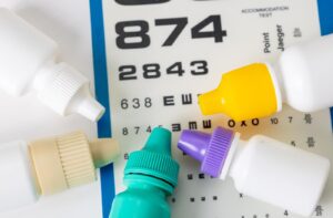 Several different colored bottles of eye drops arranged in a semi-circle on top of a vision test chart.