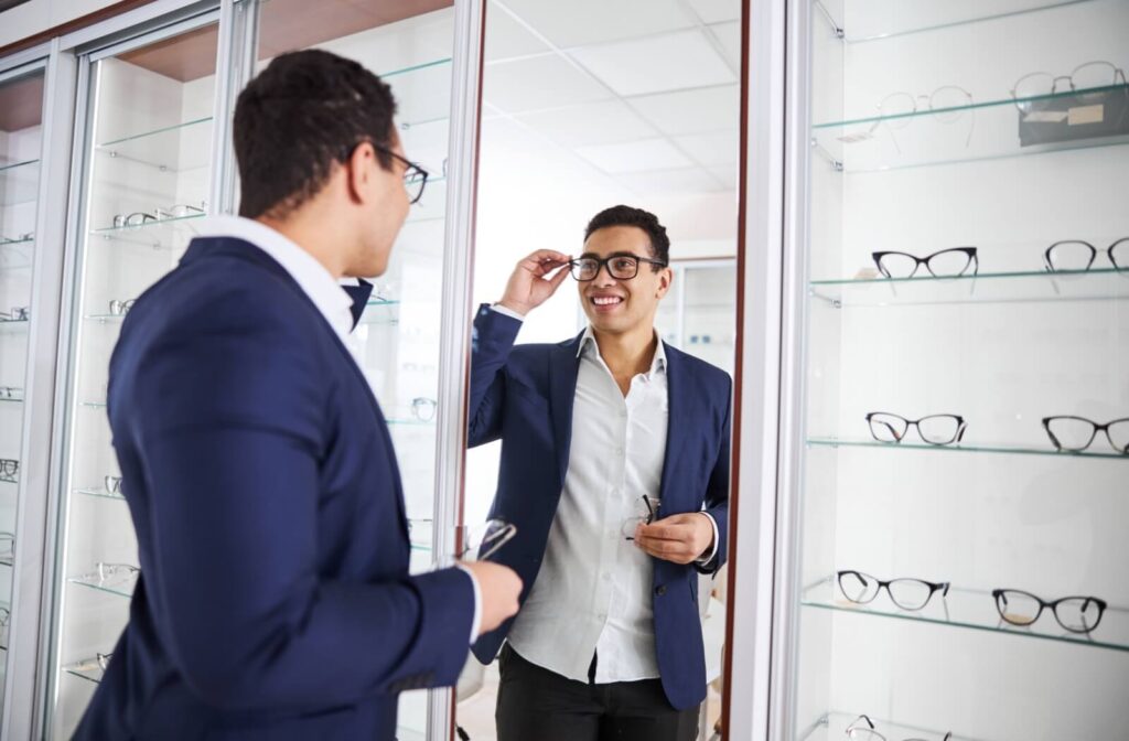 A smiling adult tries frames on in their eye doctor's showroom.