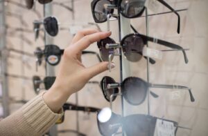 Close-up of a hand selecting sunglasses from a display rack in an optometry clinic.