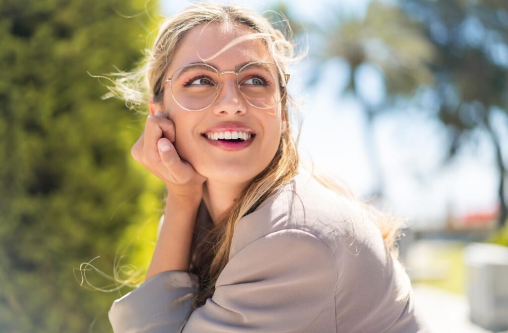 A smiling person wearing stylish, thin-rimmed circular glasses outdoors, illustrating the top female eyeglass trends for 2026.