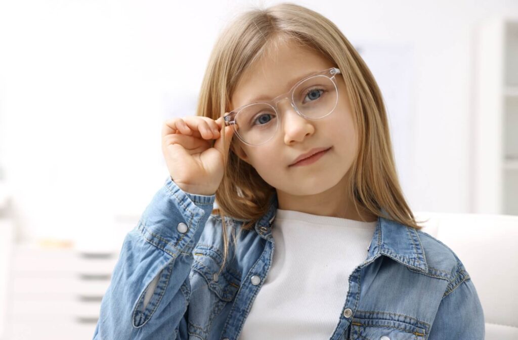 A child wearing clear-framed eyeglasses and a denim shirt while adjusting their frames.